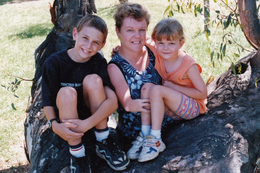 Lisa McManus poses for a photo with her two young children as they sit in a tree.