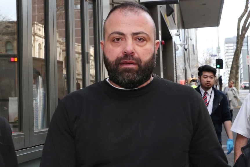 A man in a black jumper, with a beard, walks outside court.