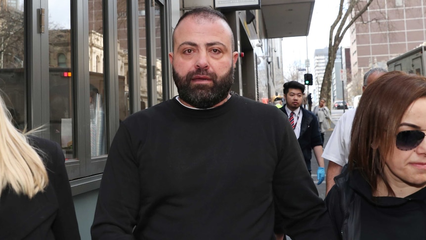 A man in a black jumper, with a beard, walks outside court.