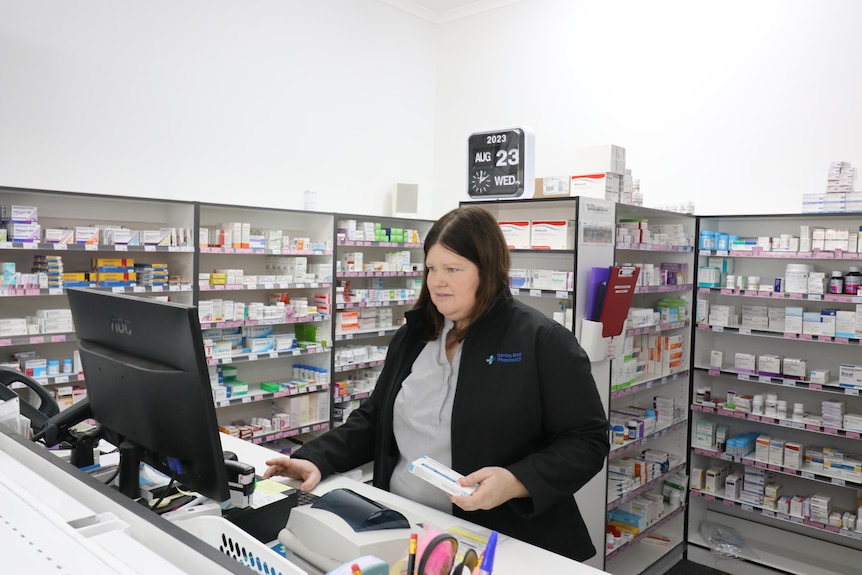 Tiffany Hibble standing behind counter with prescription medicine in hand and wall of medicines behind her.