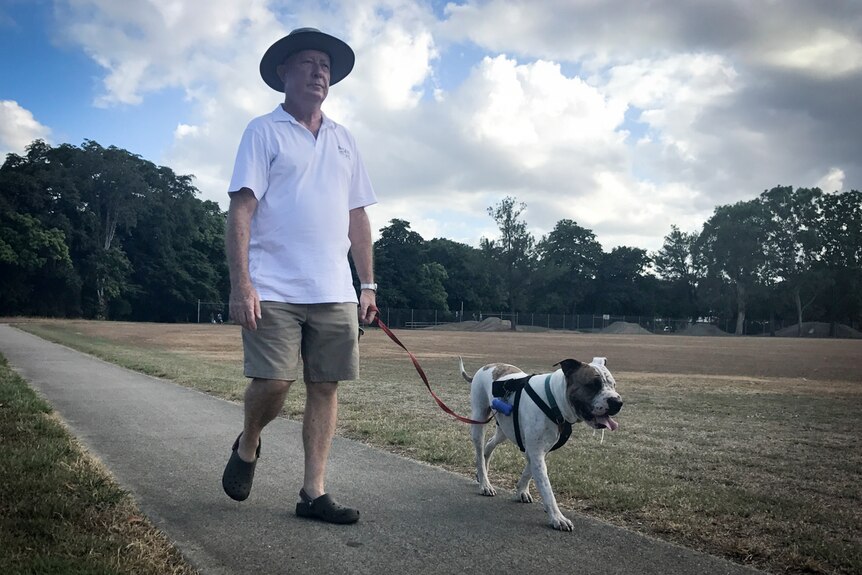 A man walks a larger dog along a path with browning grass on either side.