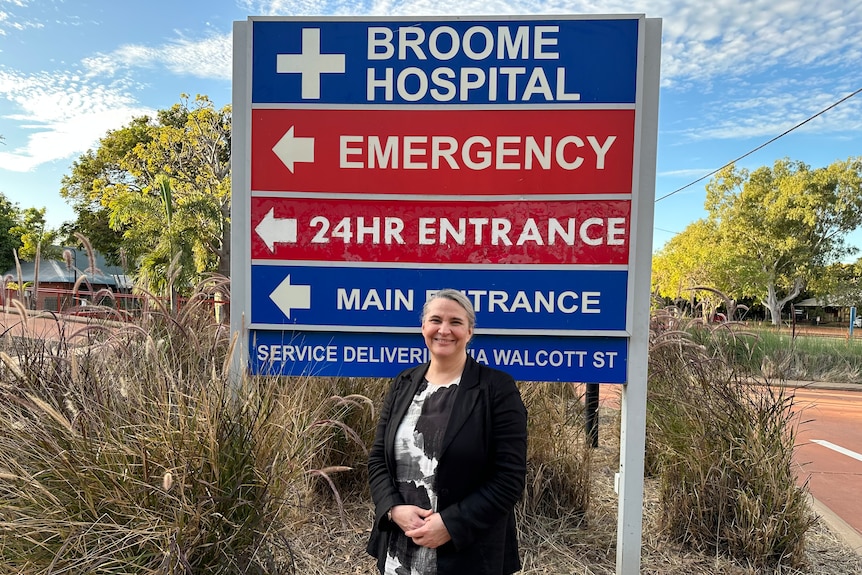 A woman stands in front of a hospital sign