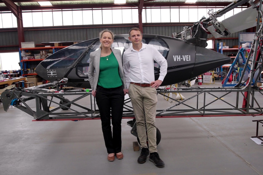A man and a woman stand in front of an electric aircraft inside an airplane hangar