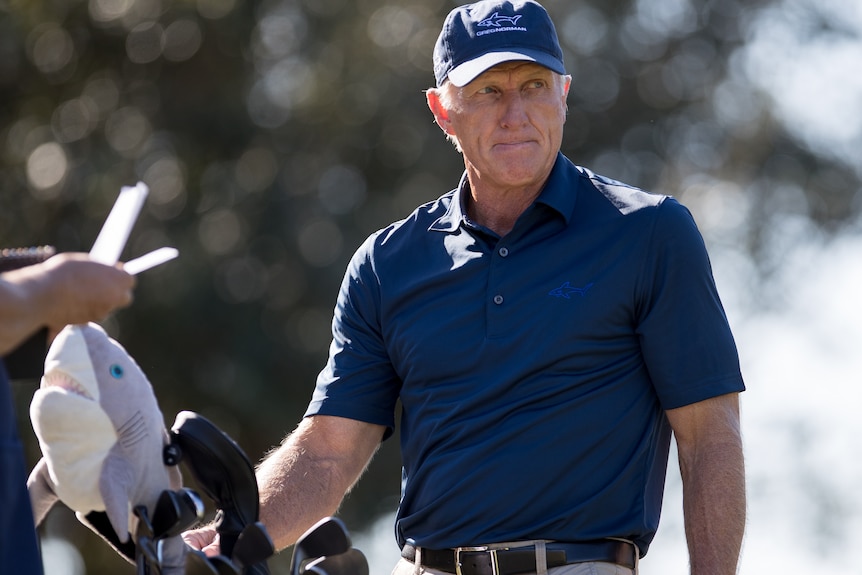Greg Norman looks down the street as he reaches into his bag for a stick.