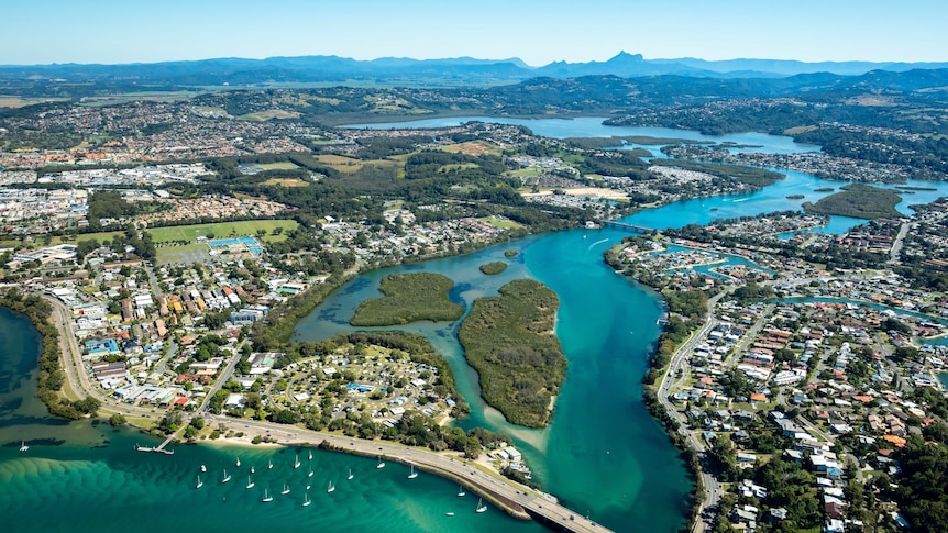 An aerial photo of an urban area with a river through the middle, and a green mountain range in the distance.