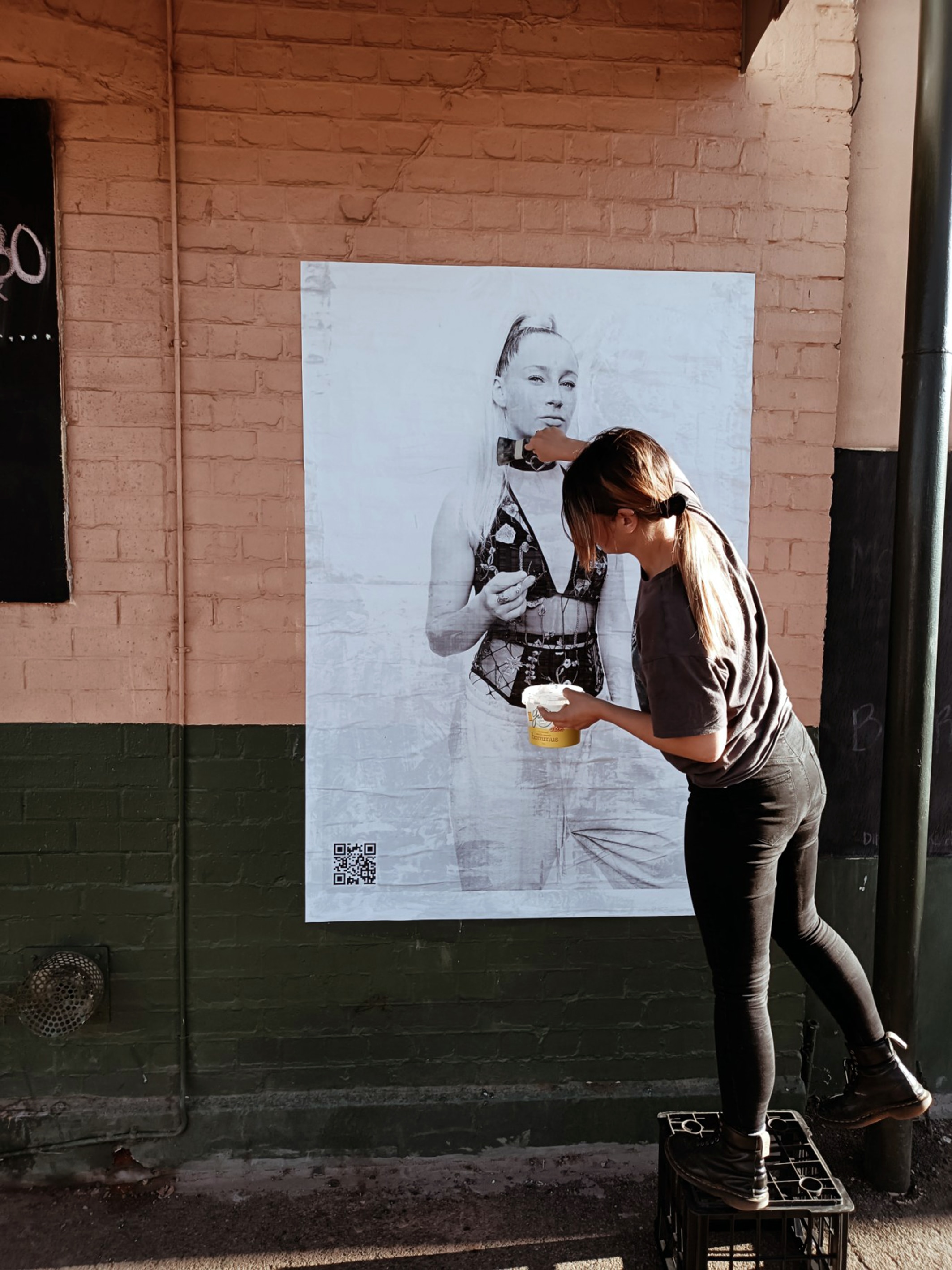 A woman pasting a black and white poster of a girl in lingerie to the wall