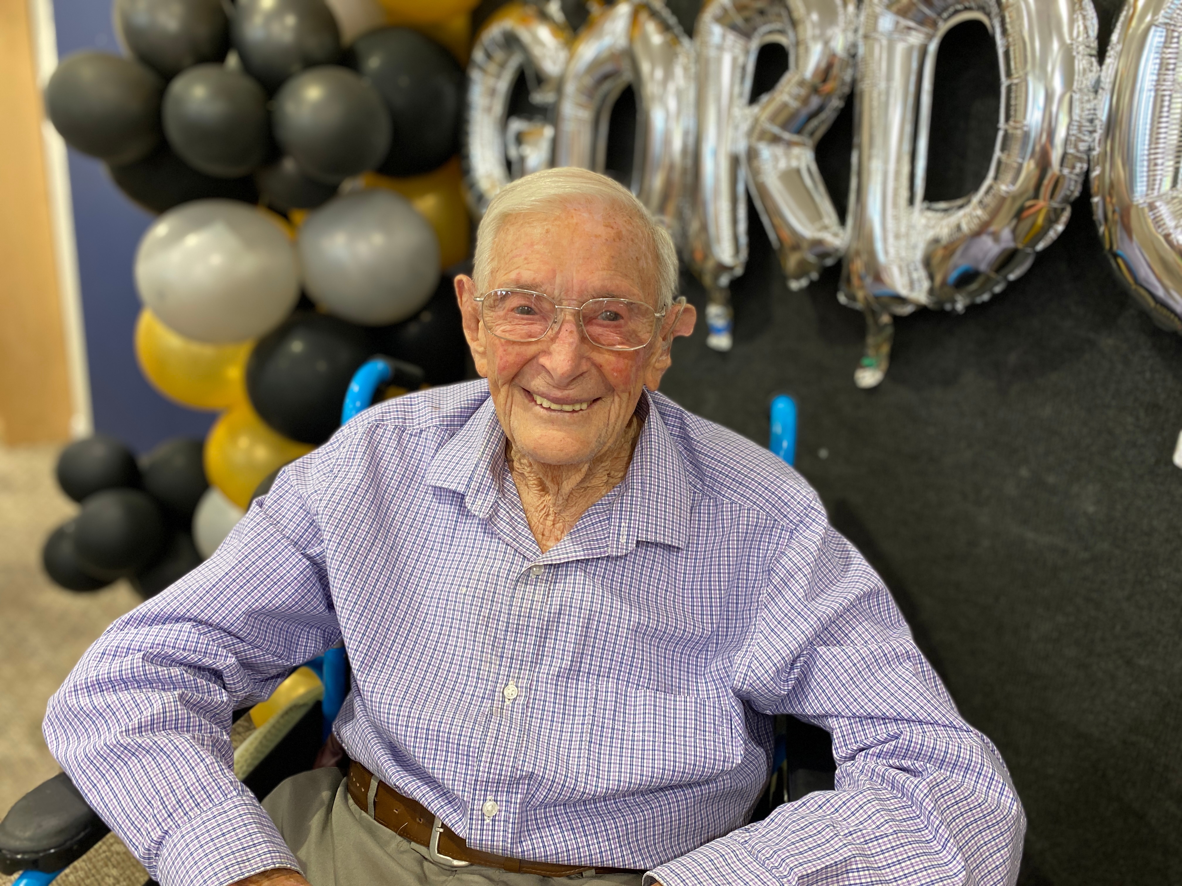 An elderly man in a check shirt sitting in front of a balloon display.