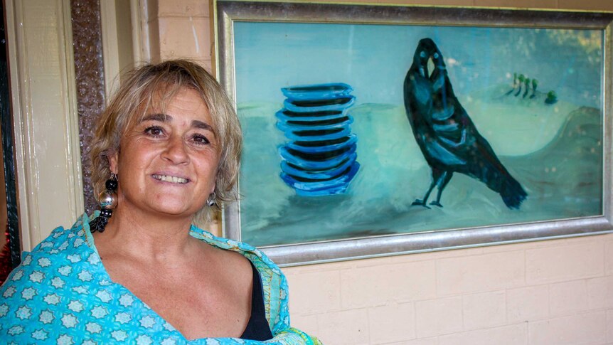 A woman poses beside a painting of a bower bird and a stack of dishes.