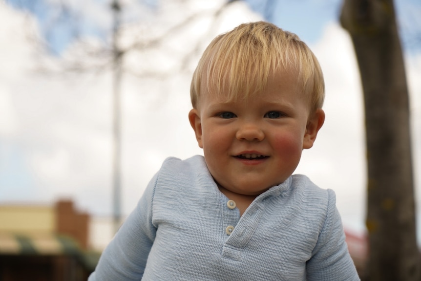 A baby with blond hair smiles at the camera.