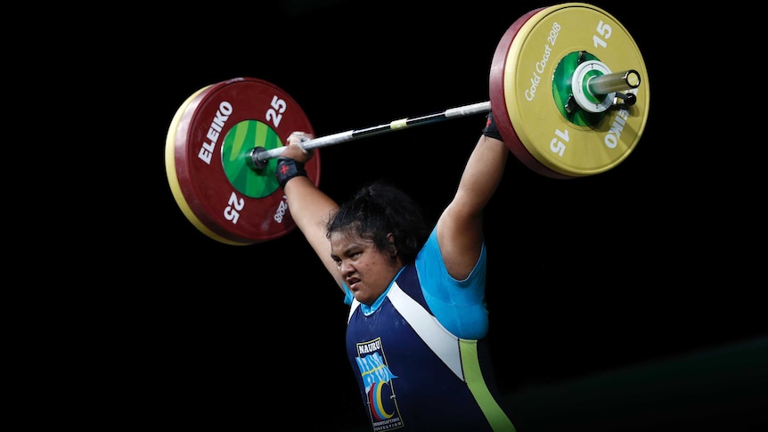 A woman with black hair lifting large weights above her head.
