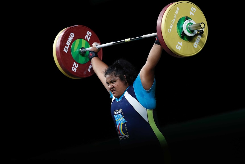A woman with black hair lifting large weights above her head.