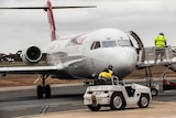 A jet plane on the tarmac as air crew move a ladder into position for disembarkation.  