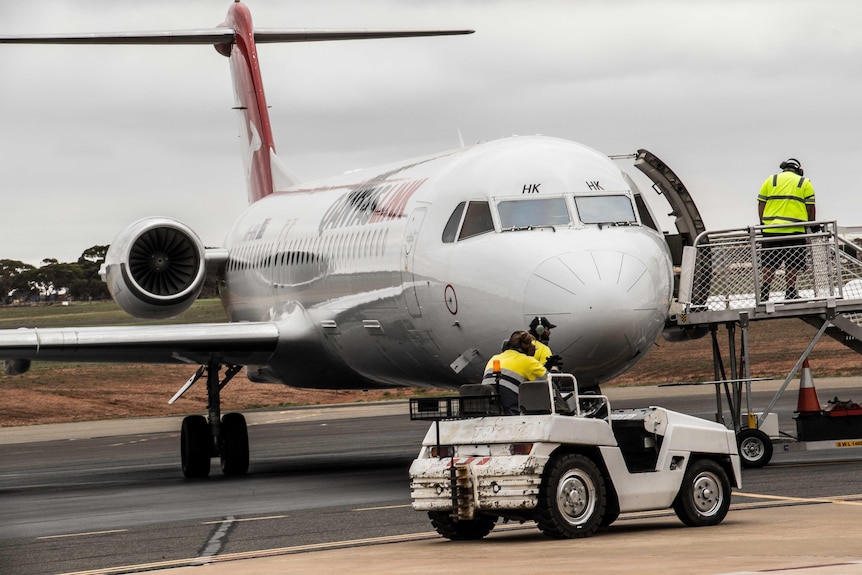 A jet plane on the tarmac as air crew move a ladder into position for disembarkation.  