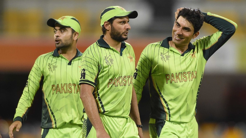 Shahid Afridi stands next to two teammates in lime-green wearing a green cap