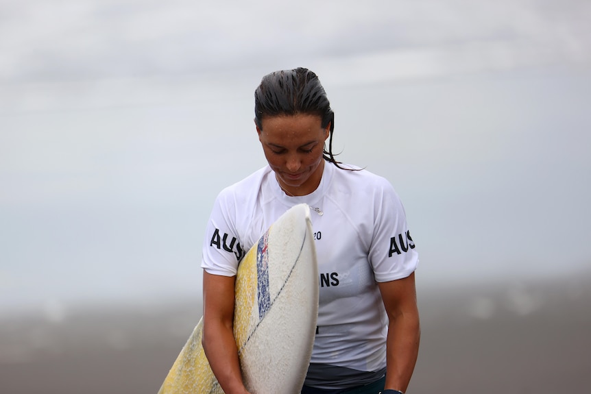 Sally Fitzgibbons looks down while carrying her surfboard