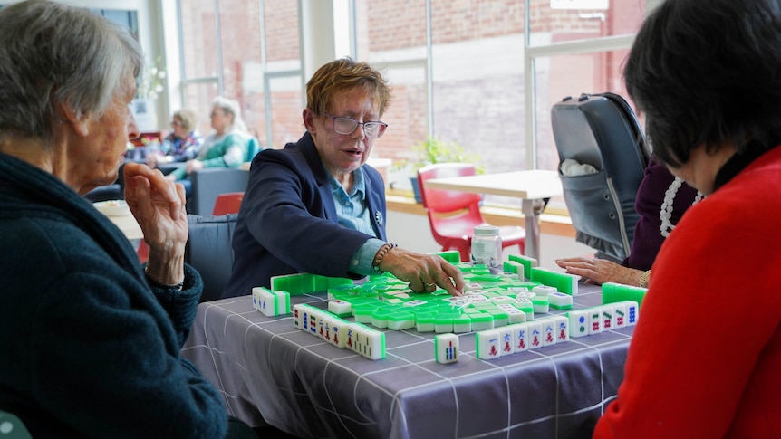Three women playing mahjong at a table. A fourth player is not visible in the photo