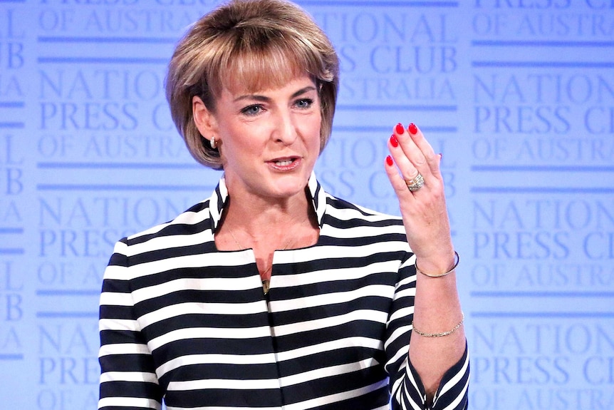 Michaela Cash raises her left hand as she addresses the audience at the National Press Club.