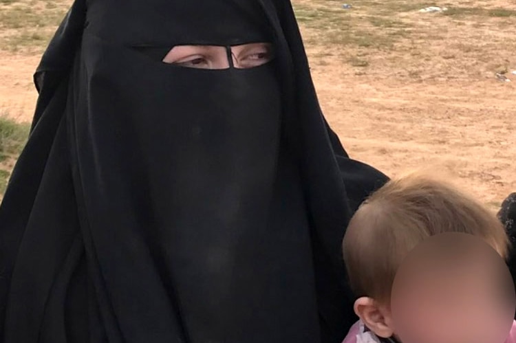 Zehra stands in a field with three women and a teenage boy. She wears a Niqab and holds a child.