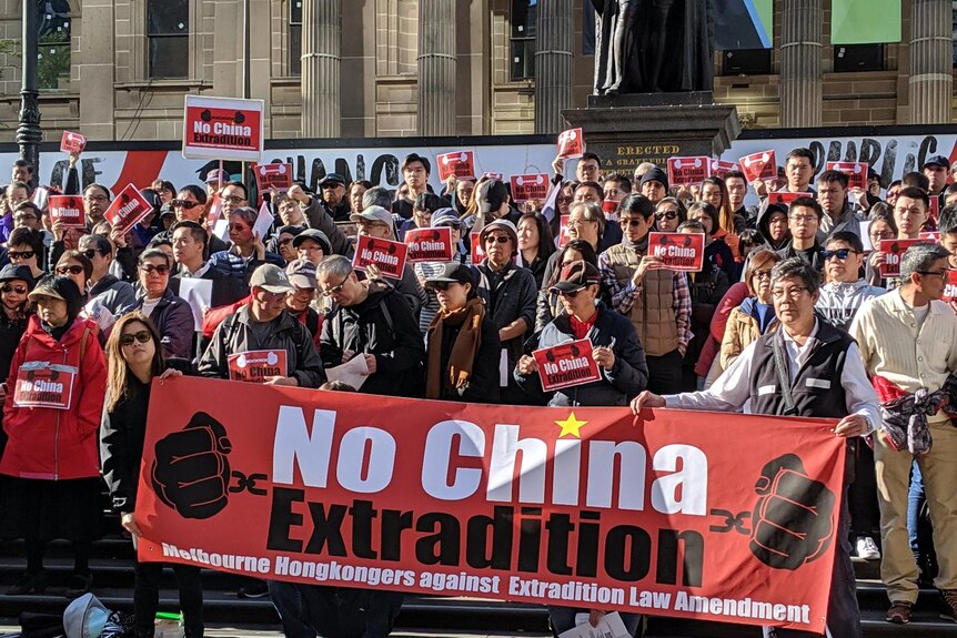 Thousands of people stand in a city street holding signs that reads "No China Extradition".