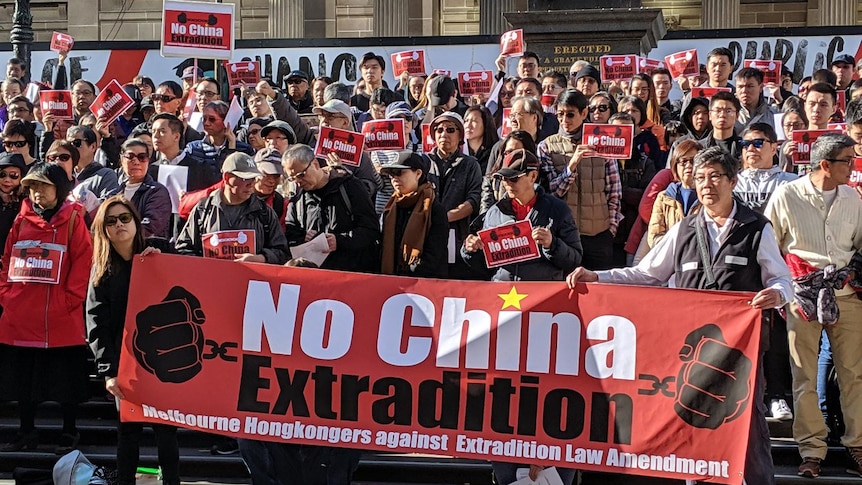 Thousands of people stand in a city street holding signs that reads "No China Extradition".