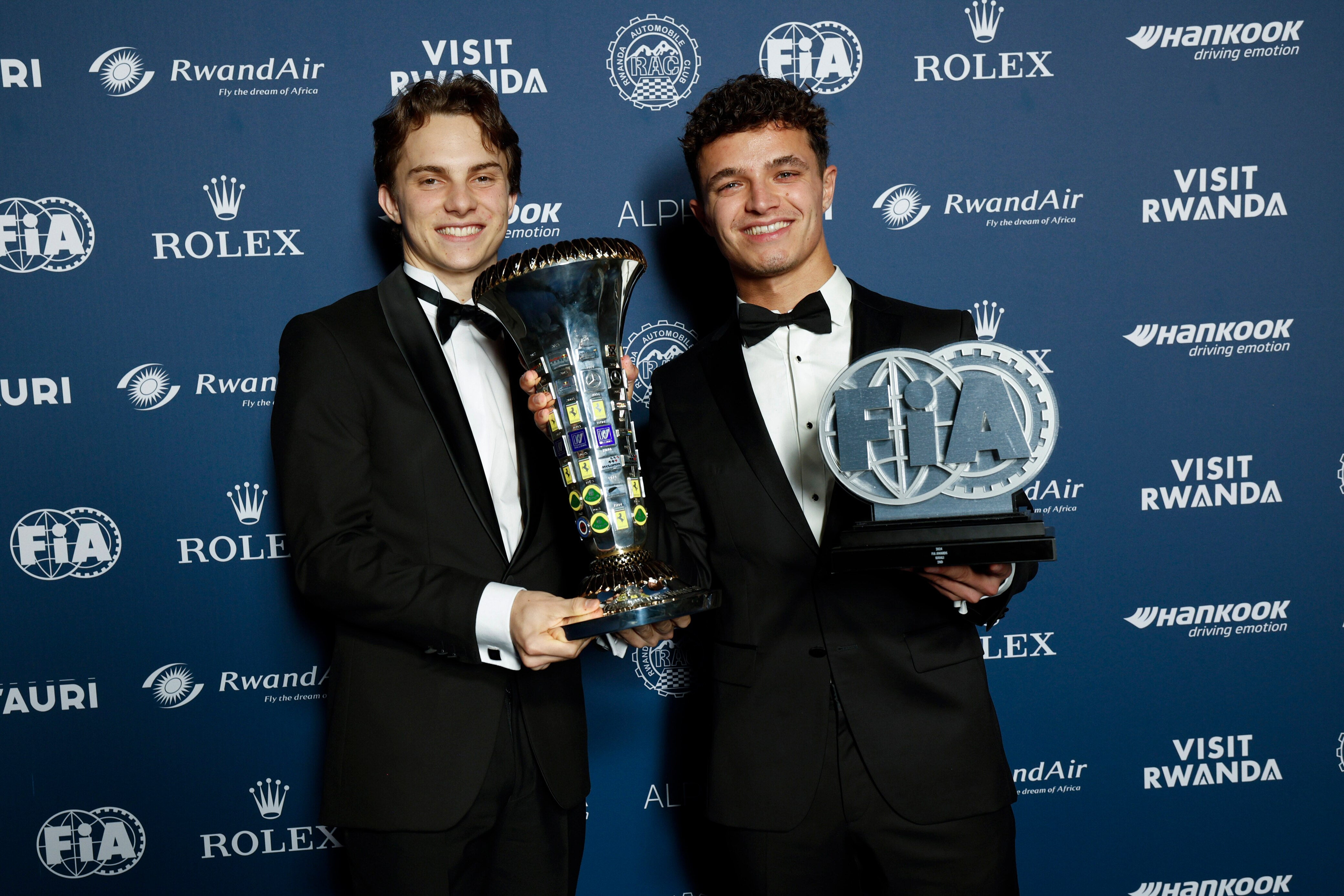 Oscar Piastri and Lando Norris in tuxedos posing with the Formula 1 Constructors' Championship trophies at the FIA Awards.