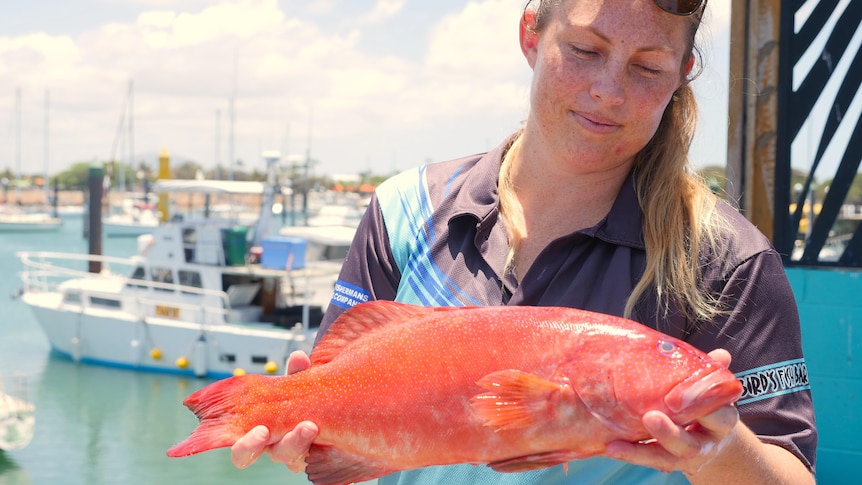 fisherwoman chloe bauer holds a coral trout in front of marina