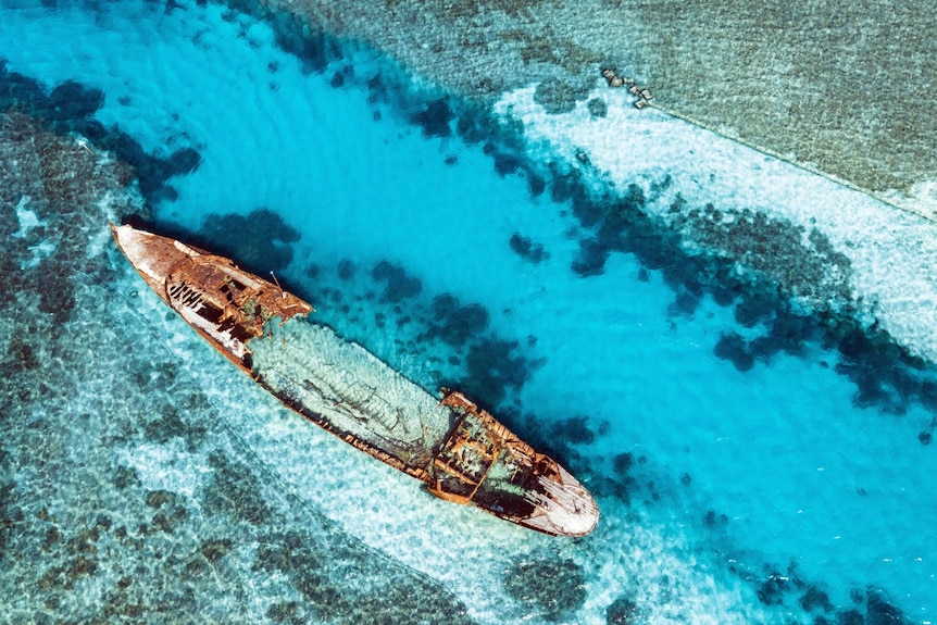 Channel blasted through reef, big shipwreck on left side, birds eye view, clear water.