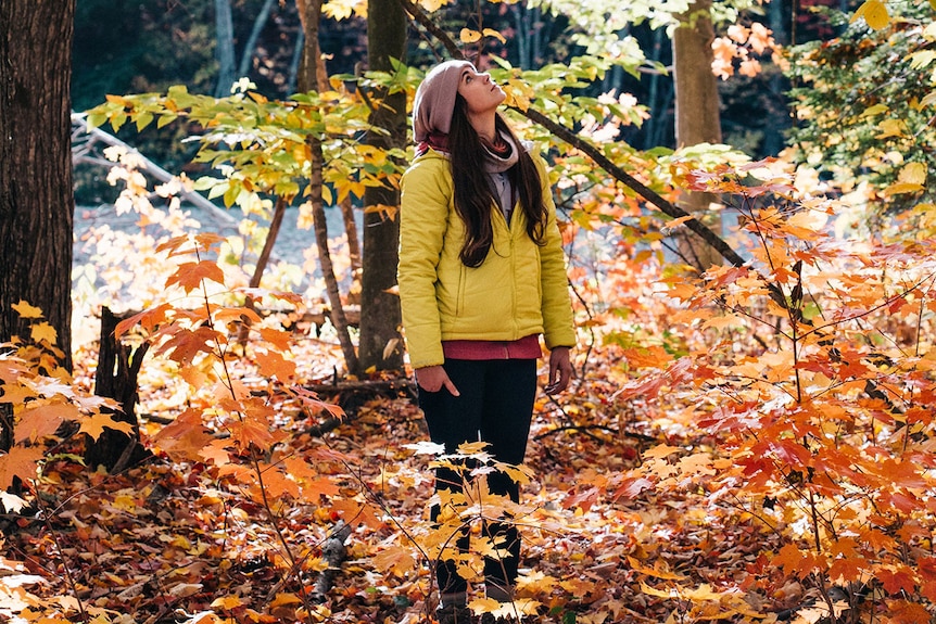 Woman surrounded by autumnal-coloured trees with leaves falling.