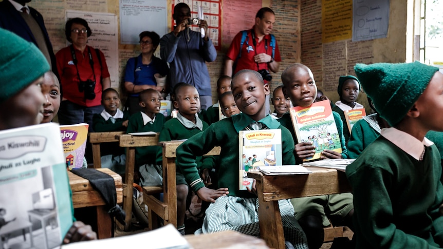 A Kenyan girl in school uniform smiles at the camera while holding up a text book.