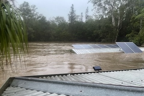 Brown flood waters with solar panels on the top of roofs visible