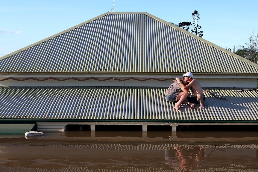 A man comforts his daughter on the roof of their Bundaberg house.