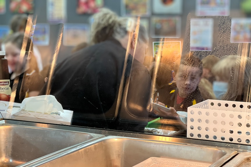 Children are served lunch, seen through the see the glass of the bain marie