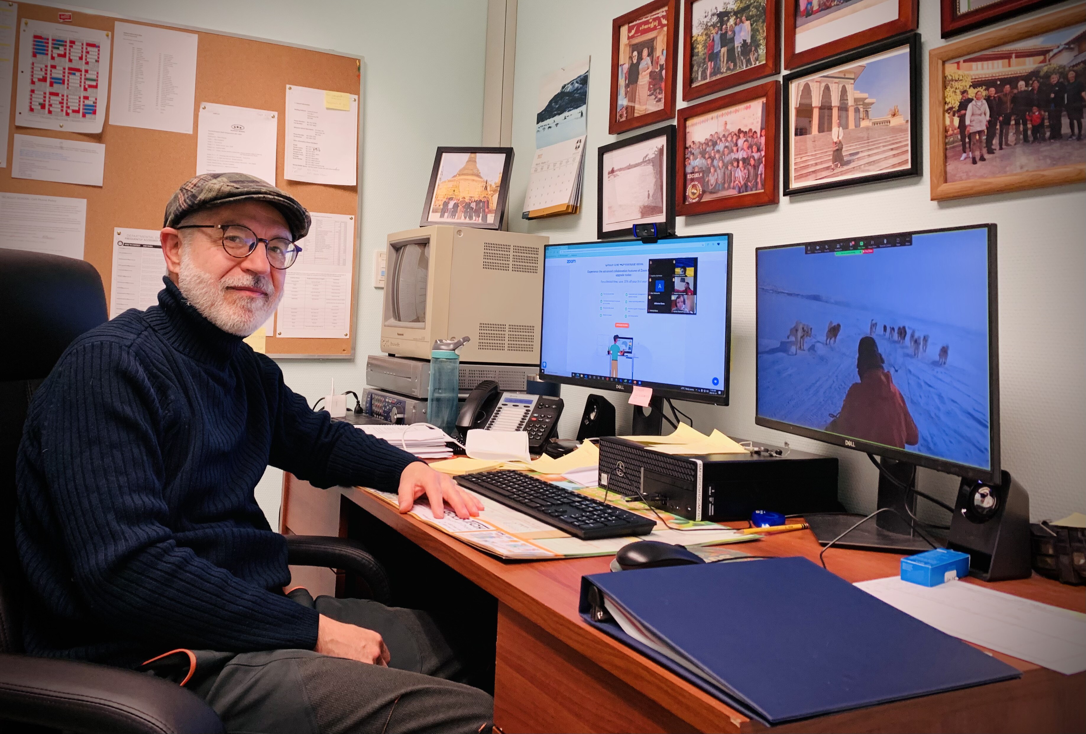 An older man sitting at his desk with two computer monitors looking at the camera