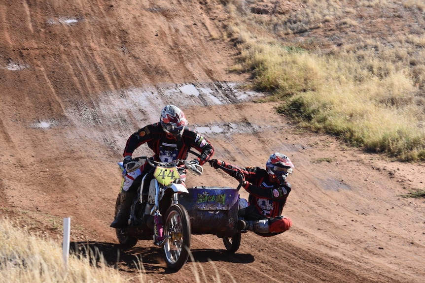 Two riders in orange on a motorbike and sidecar. The sidecar rider is leaning out