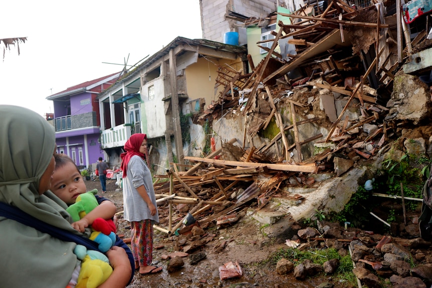 Two women inspect a building reduced to rubble. 