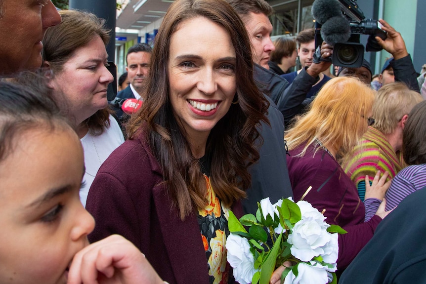Jacinda Ardern holding a bouquet of white flowers in a crowd of supporters