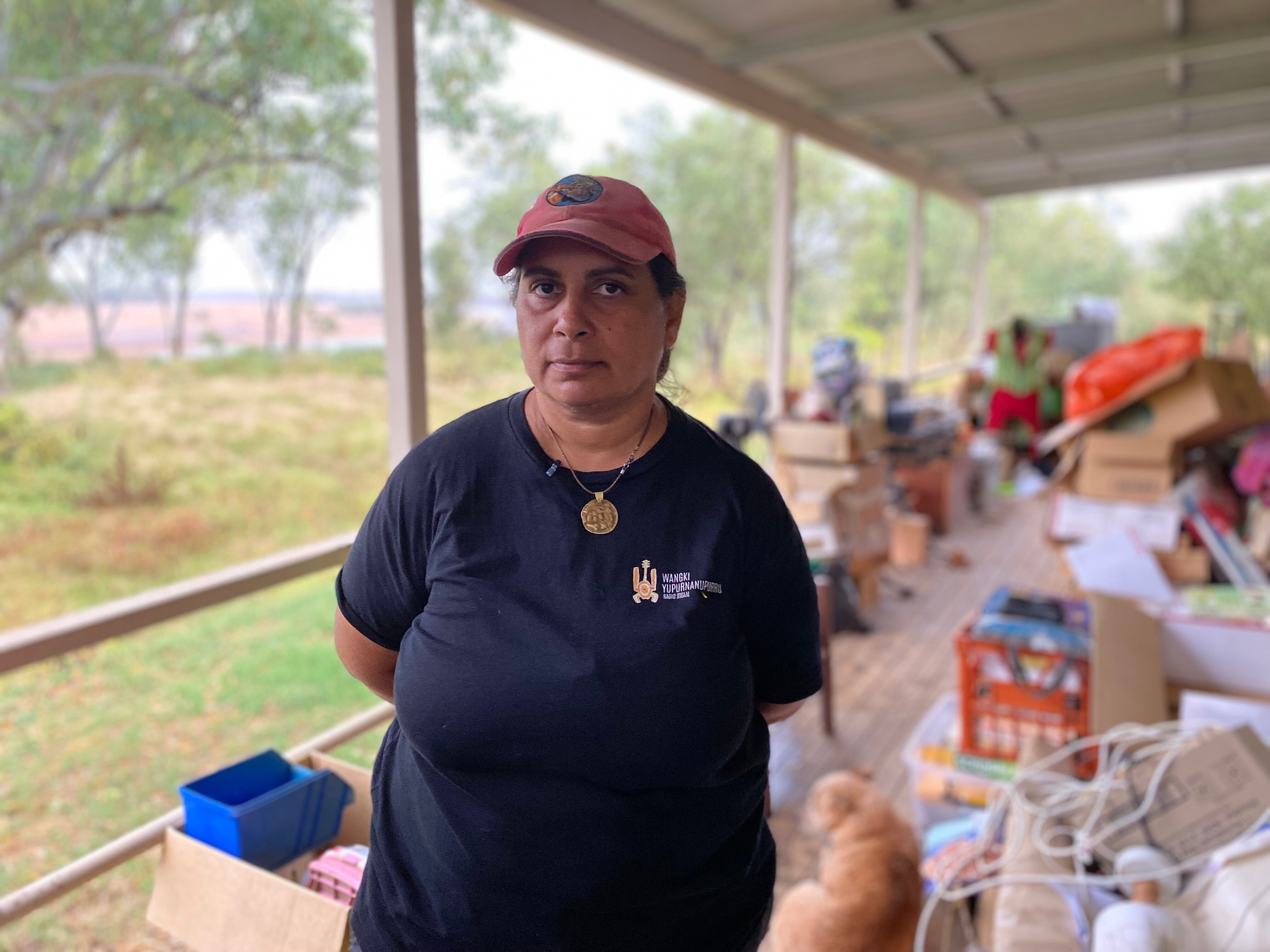 A woman with a hat on, under her deck. Flood wrecked belongings are behind her.