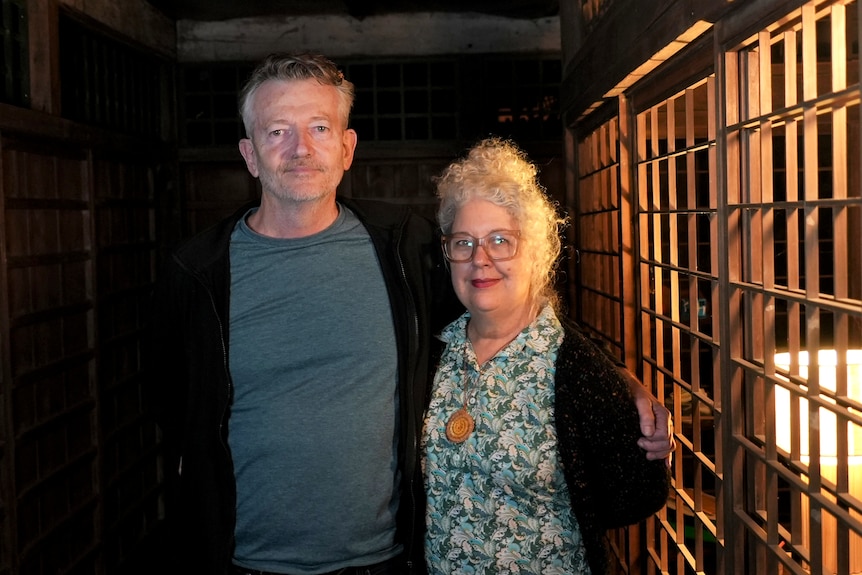 A man and woman stand in a dark corridor next to a wooden lattice wall