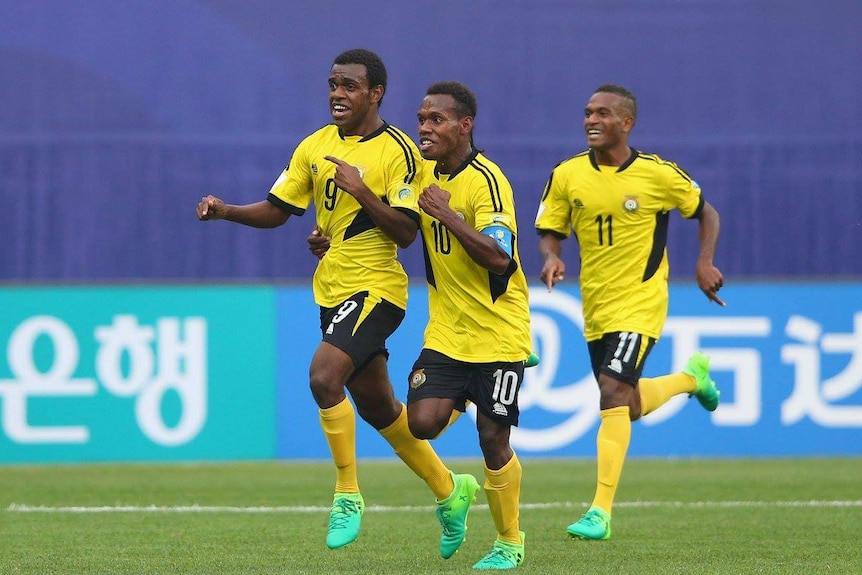 Vanuatu footballers smile and hug after scoring a goal.