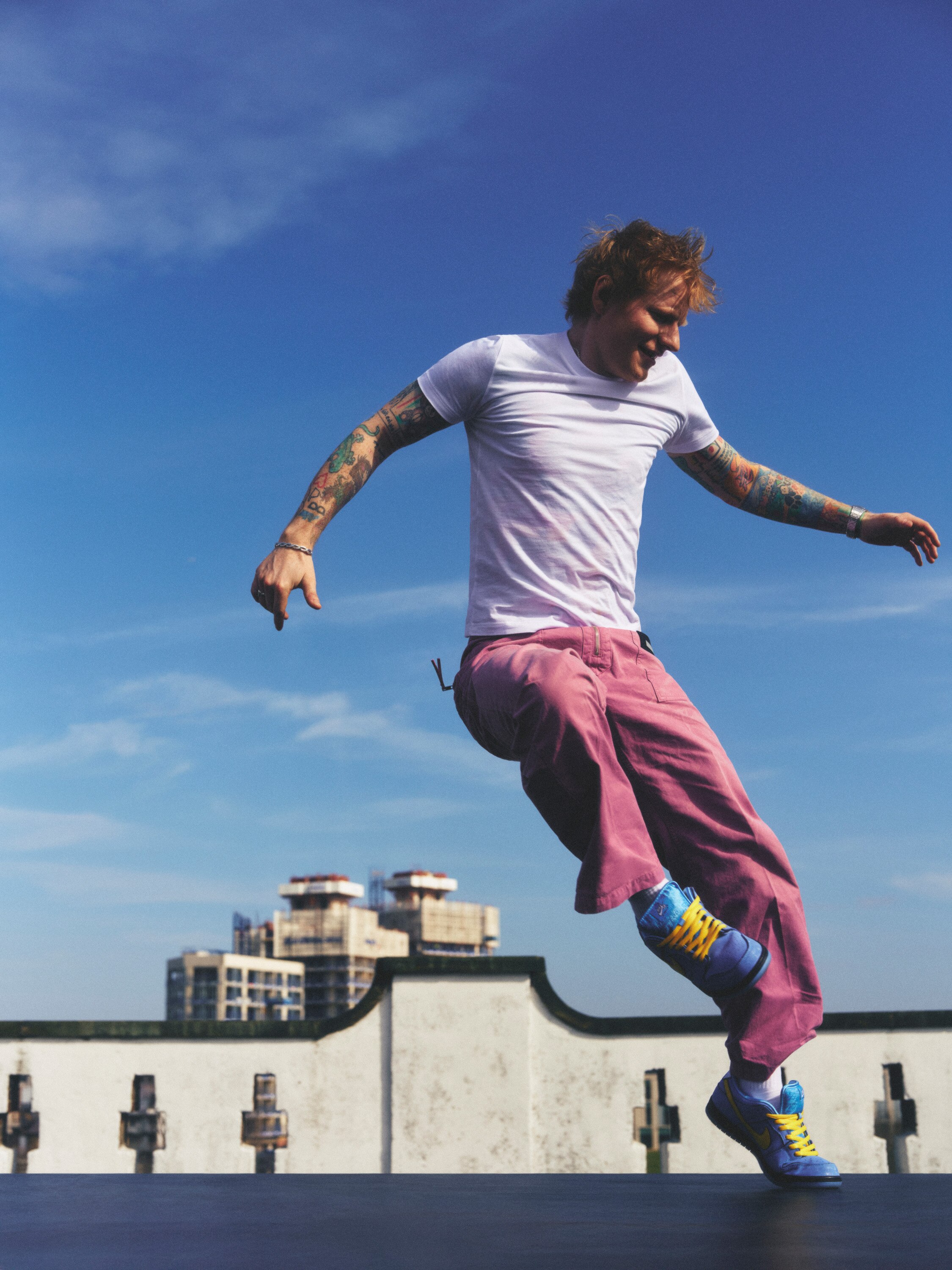A man wearing a white top and pink jeans jumps in the air