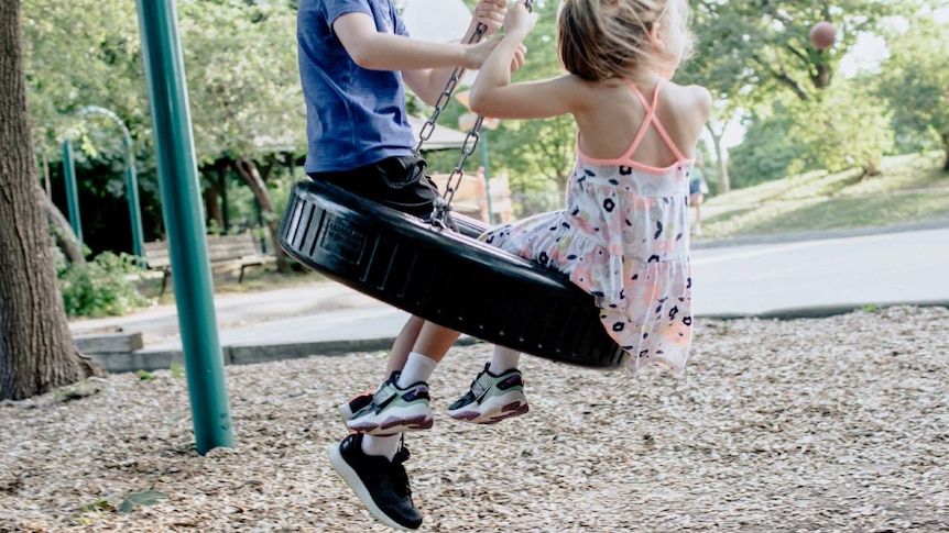 Two kids play on a swing.