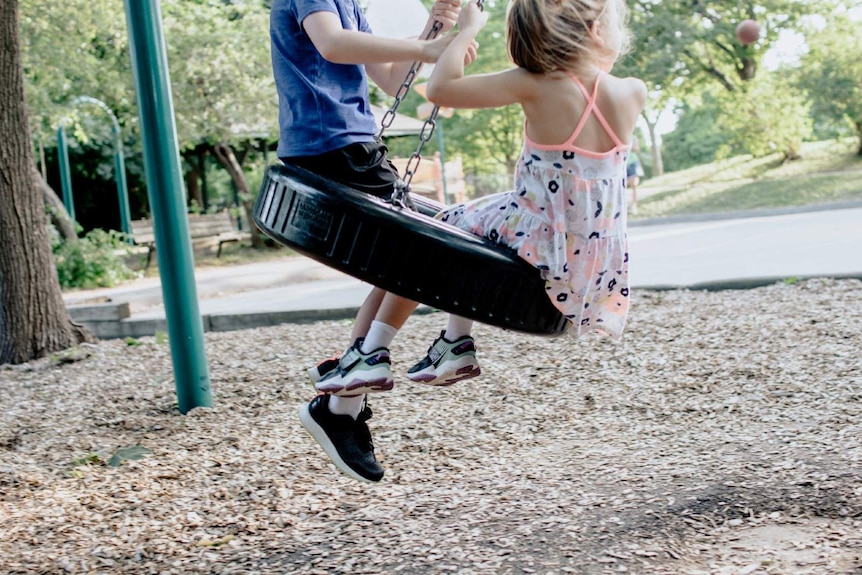 Two kids play on a swing.