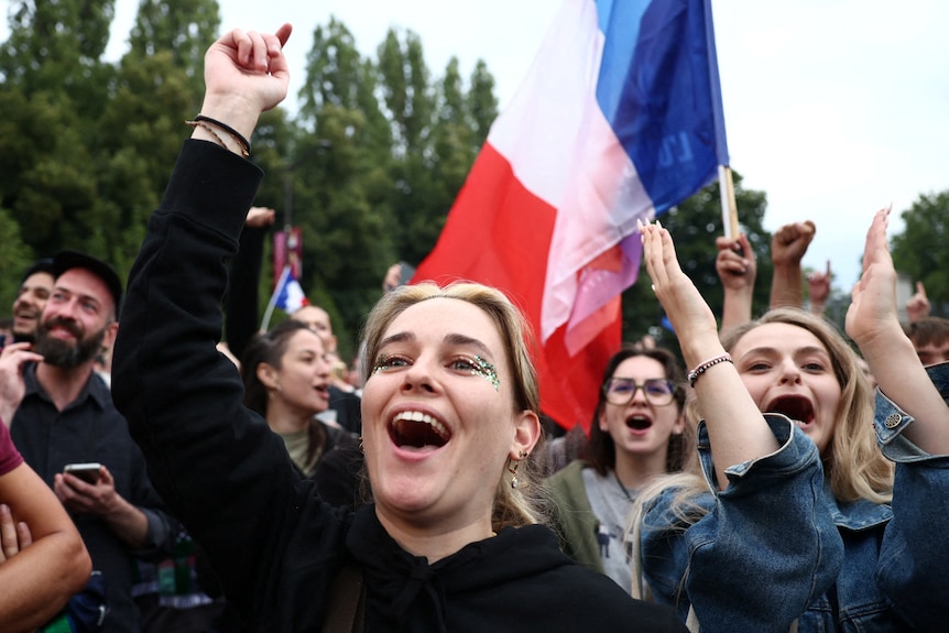 A close up of women cheering in the street as a French flag waves in the air behind them