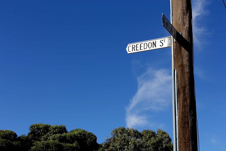 A street sign attached to a power pole, with a blue sky in the background.