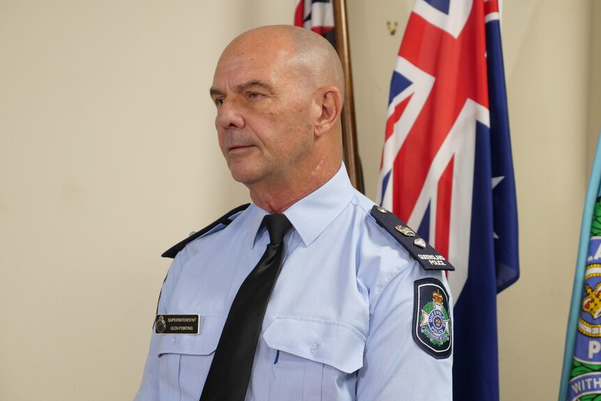 A police officer stands in uniform, in a room with the Australian flag behind him