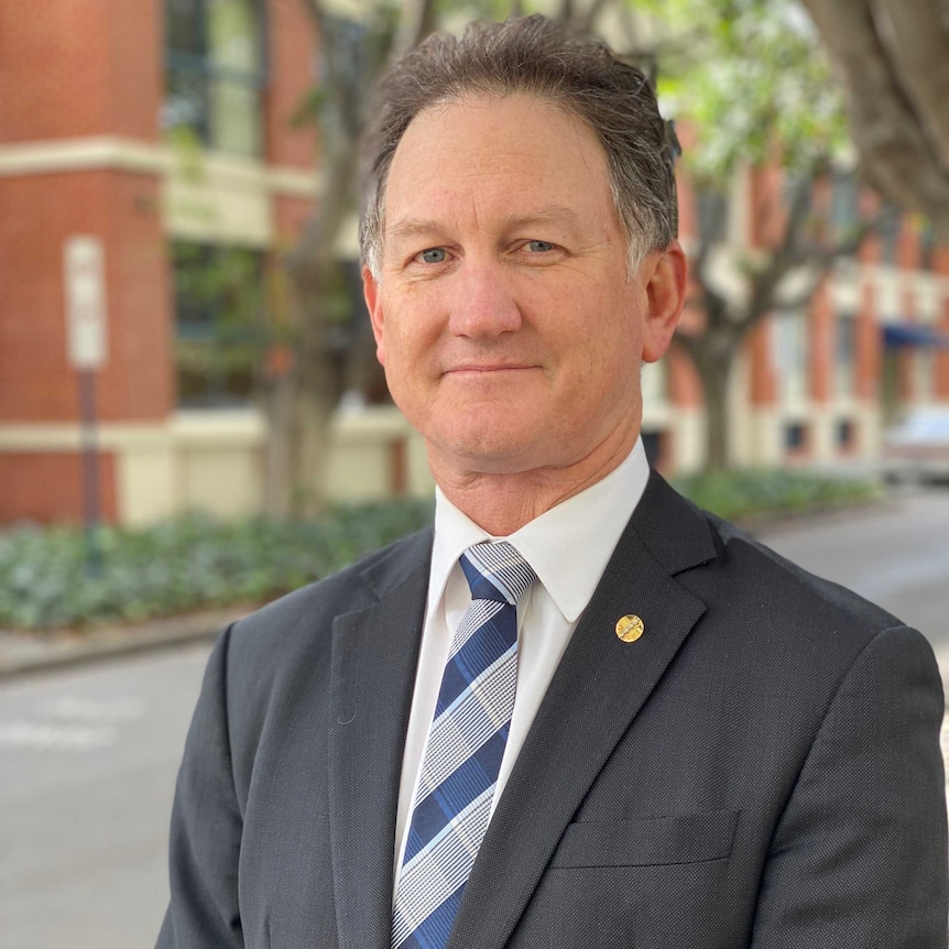Dr Michael Gannon wearing a suit and tie standing outside with trees and a building in the background.