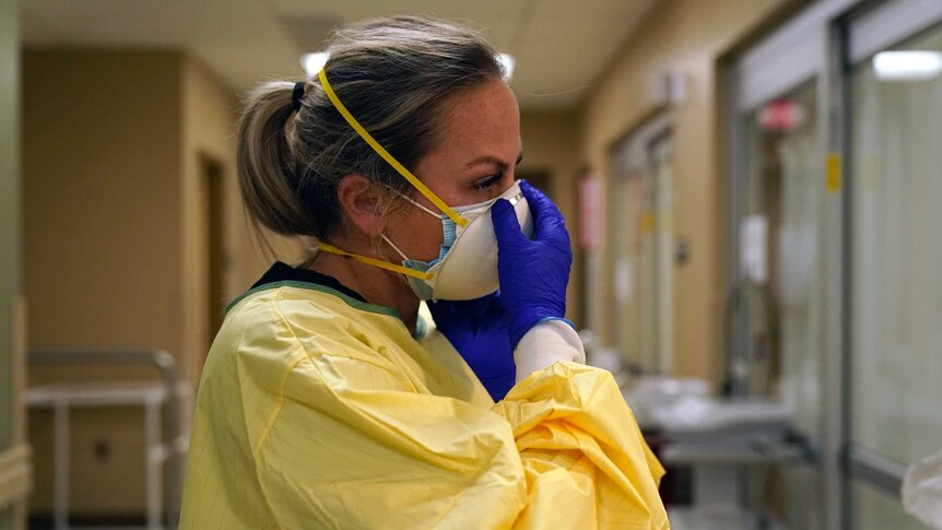 A nurse fastens her mask as she puts on PPE in a hospital ward