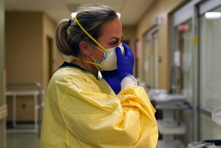A nurse fastens her mask as she puts on PPE in a hospital ward