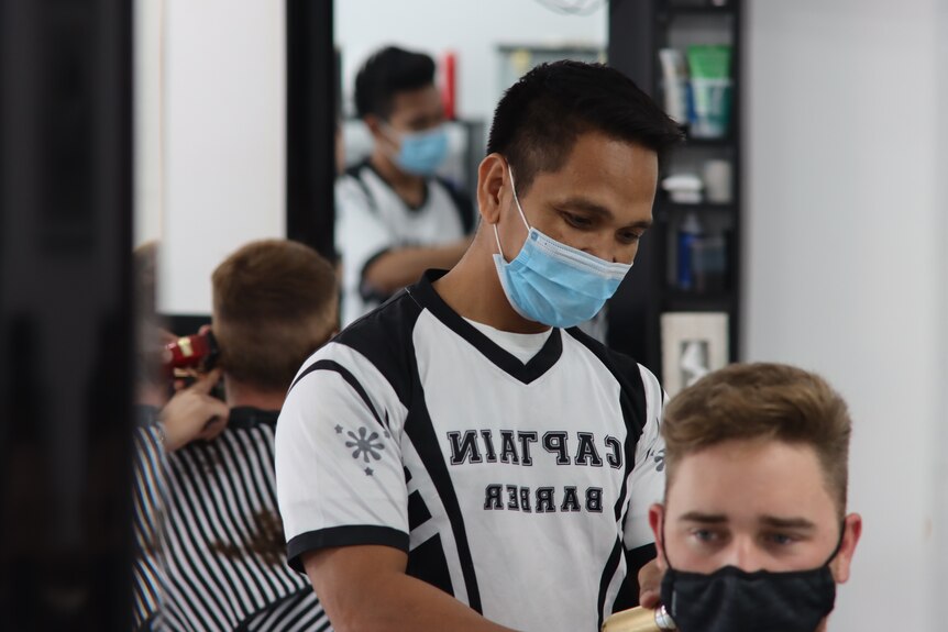 A man cuts another man's hair. Both are wearing face masks.