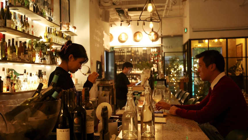 A woman works in a wine bar as a man sits at the bar.